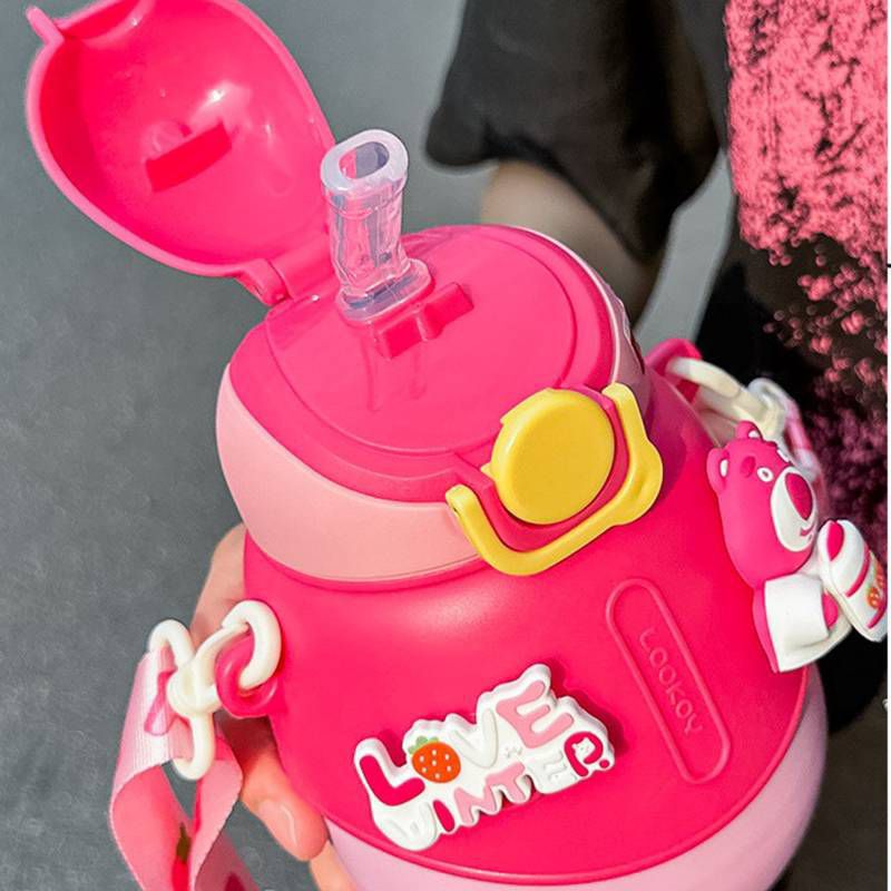 Pink children's water bottle with straw and handle, featuring a cartoon character, on a gray background.