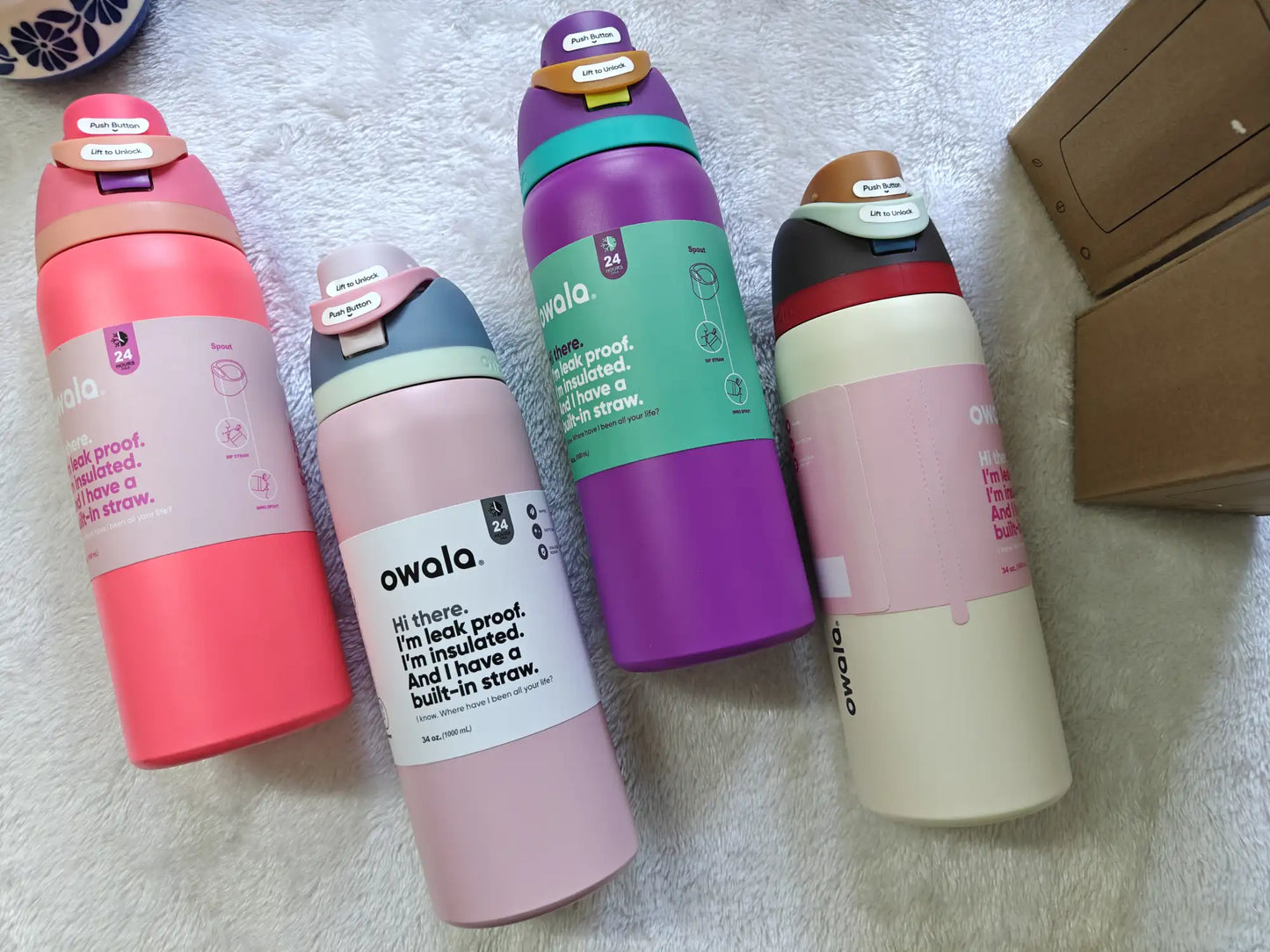 Four Owala water bottles in different colors on a textured surface.