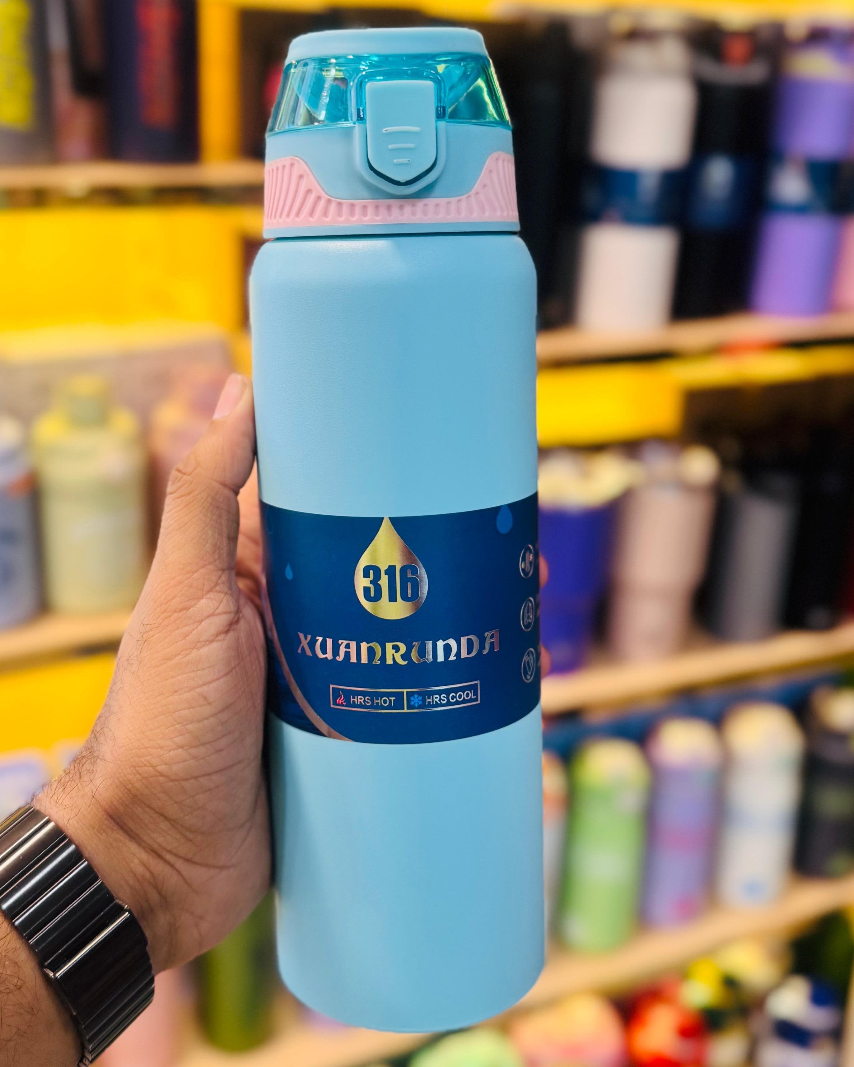 Blue thermos bottle held by a hand with a blurred store shelf in the background