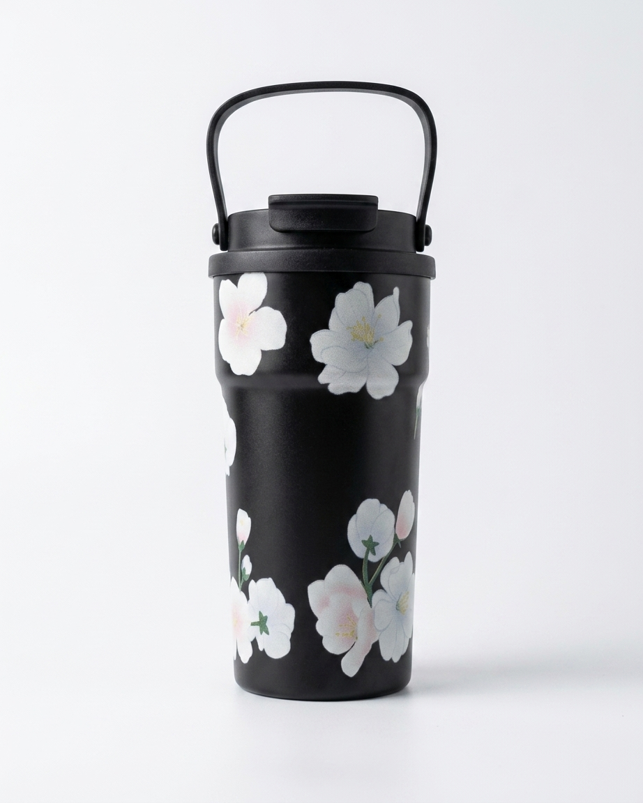 A black travel tumbler with a matching lid and carry handle, decorated with a pattern of white and pale pink cherry blossom flowers, set against a plain white background.