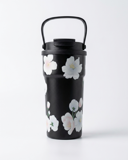 A black travel tumbler with a matching lid and carry handle, decorated with a pattern of white and pale pink cherry blossom flowers, set against a plain white background.