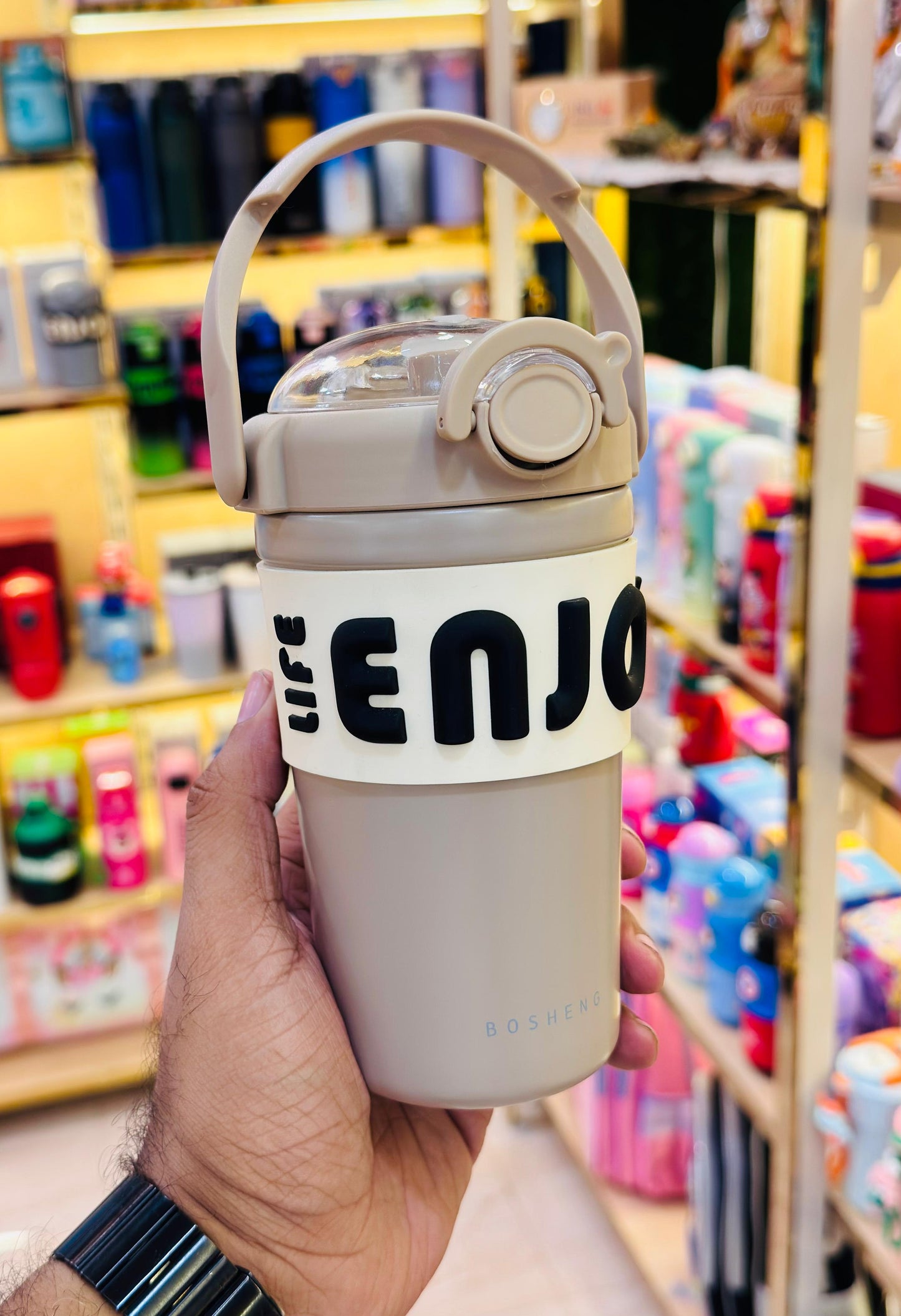 Hand holding a white tumbler with 'ENJO' branding in a store setting