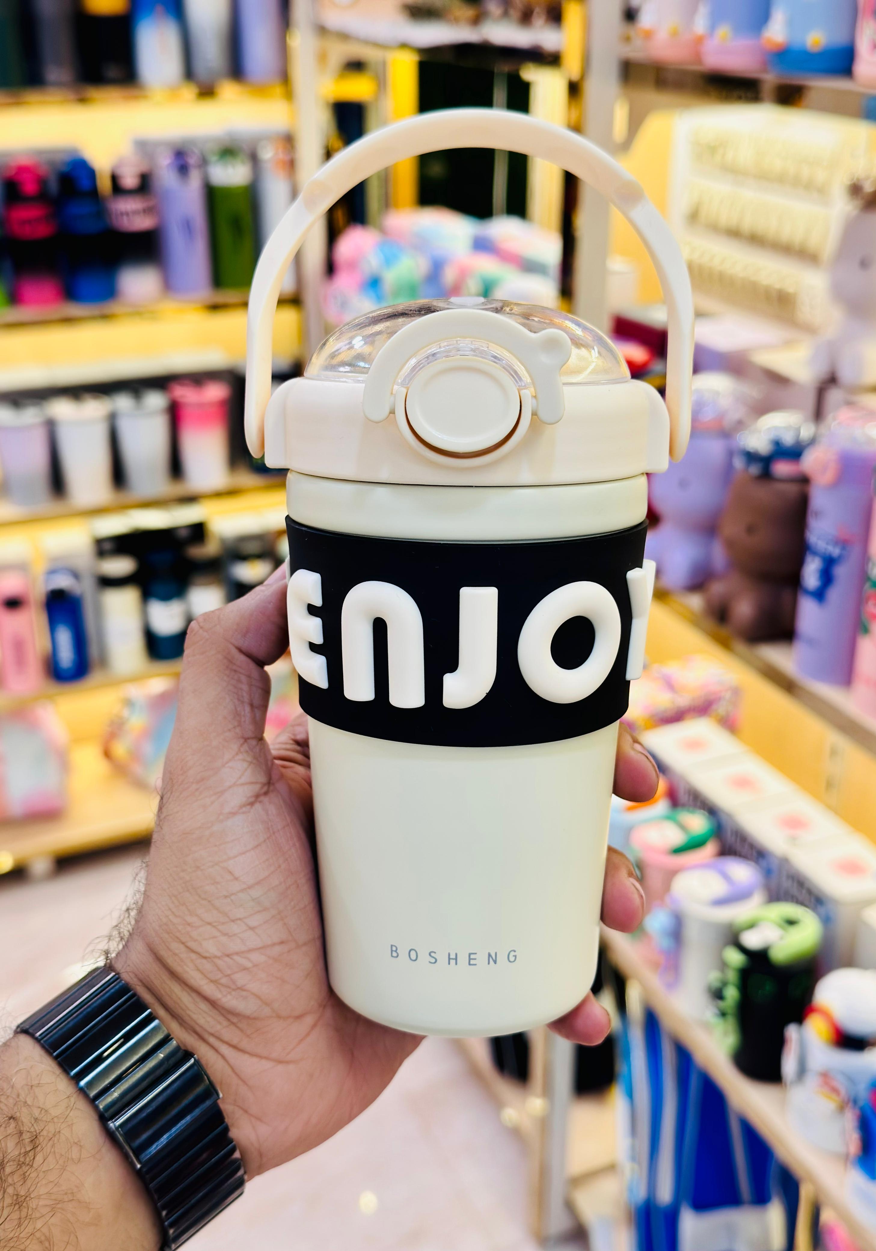 Hand holding a white tumbler with 'ENJO' branding in a store setting