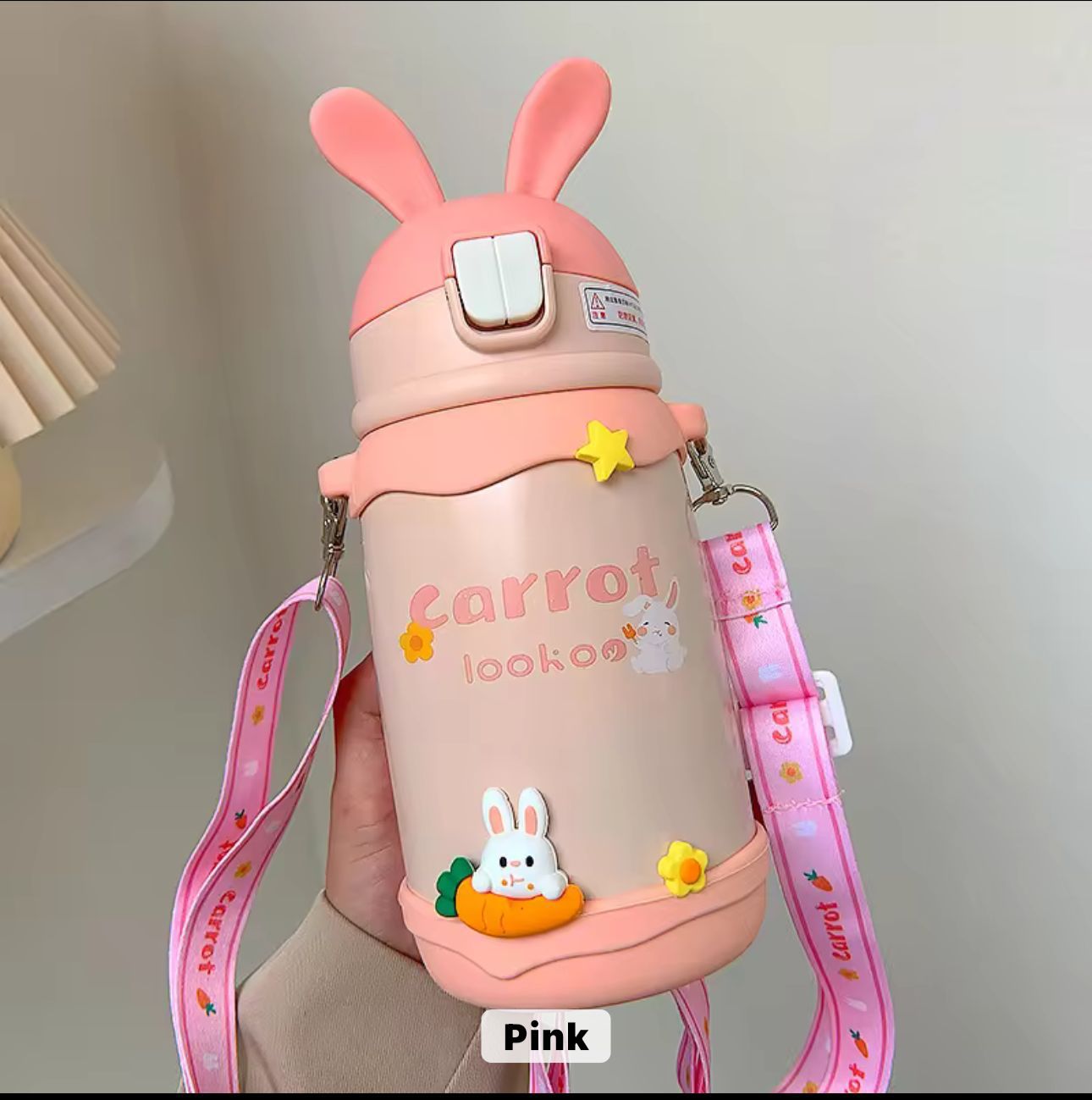 Pink water bottle with bunny design and strap on a neutral background