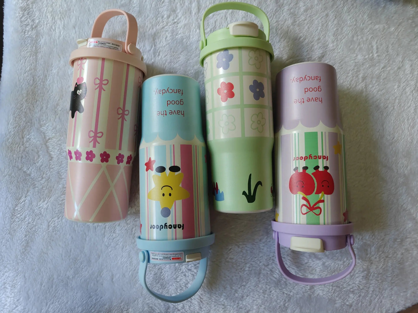 Four colorful children's thermos bottles with cartoon designs on a textured surface.