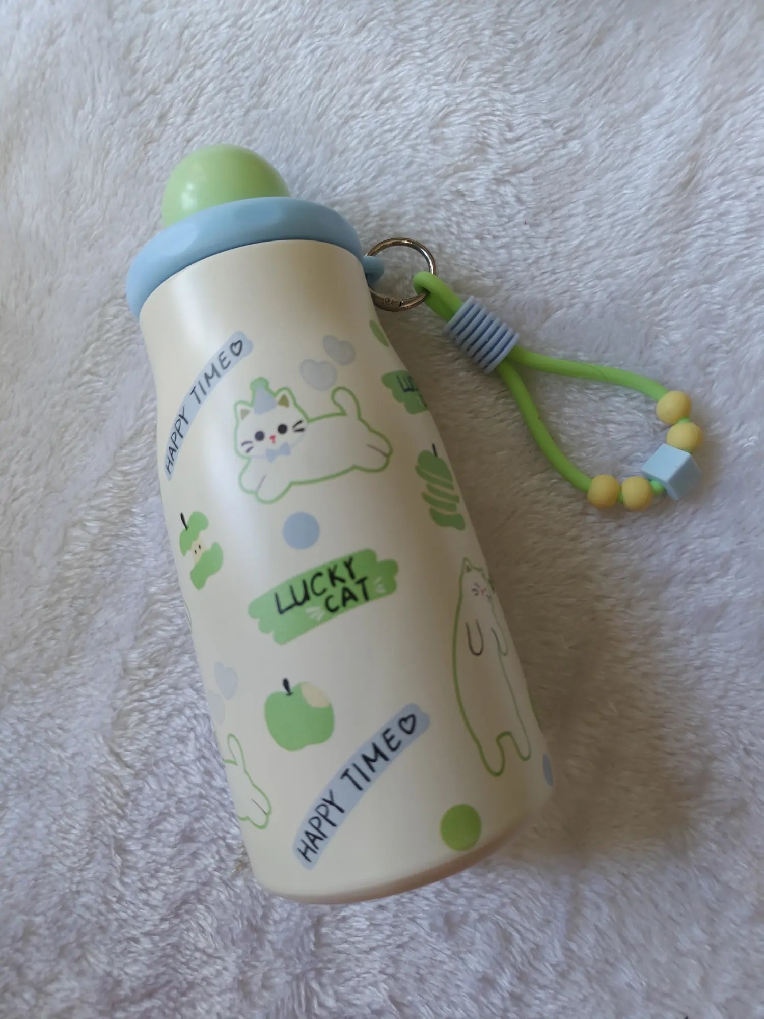 Children's bottle with green cat illustrations on a soft surface