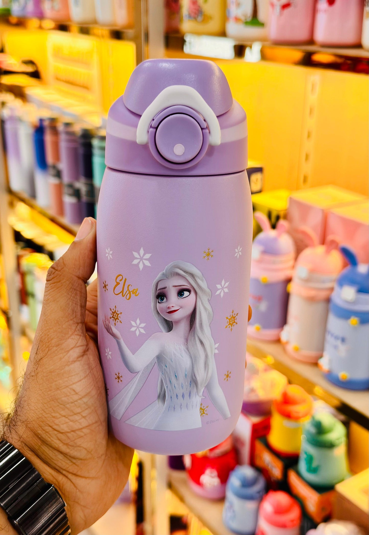 Children's purple tumbler with character design held in a hand, with a store shelf in the background.