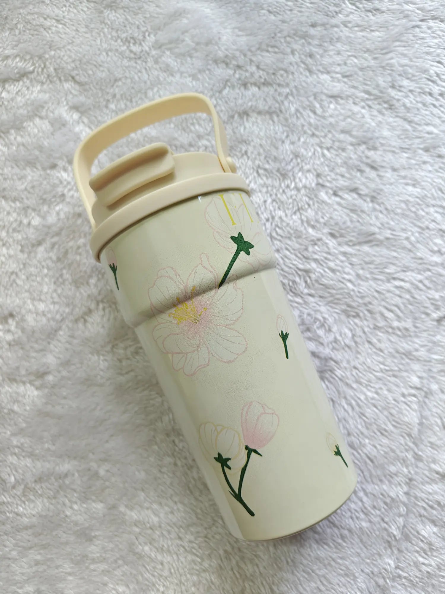 Cream-colored tumbler with floral design on a white fluffy surface