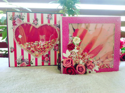 Two decorative handmade picture frames with pink and red floral designs, displayed on a white textured surface with green plants in the background.