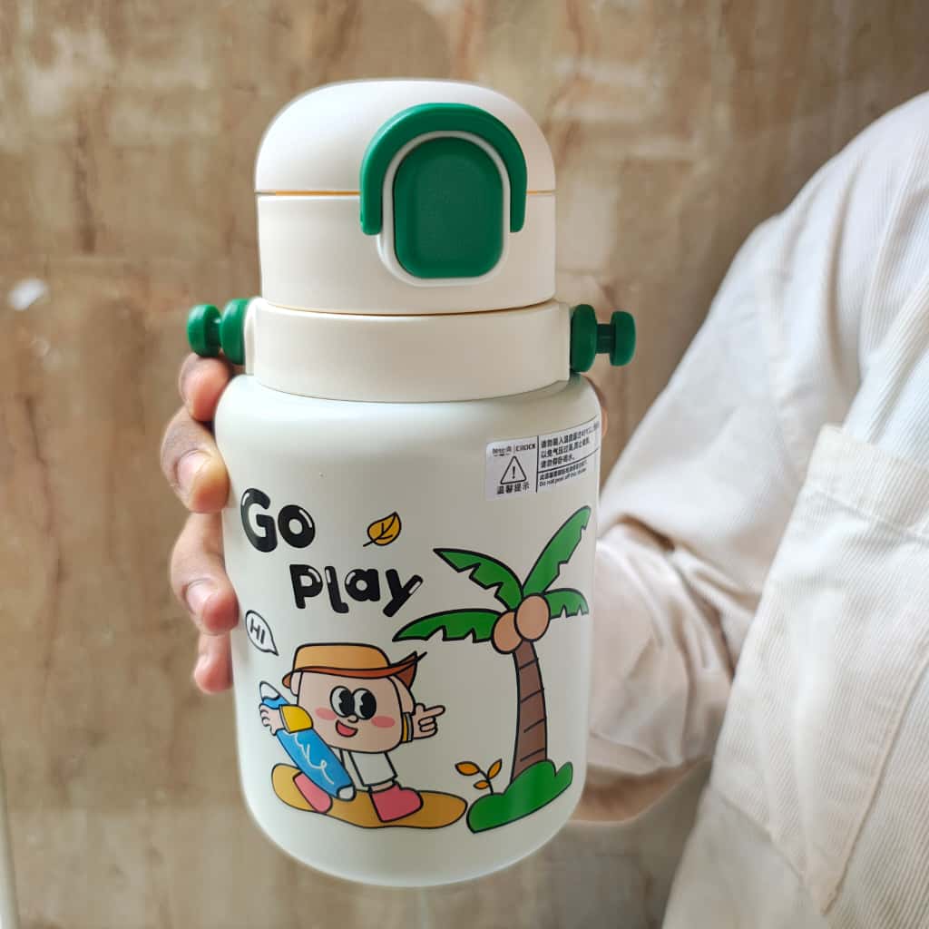 White thermos with green lid held by a person, featuring cartoon character and 'Go Play' text on a beige background.
