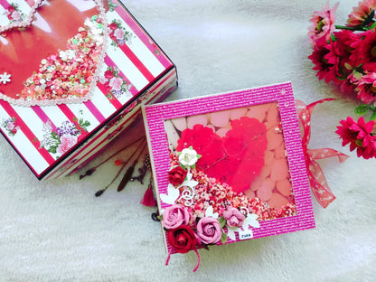 A Valentine's Day themed gift box set on a white textured background, featuring a pink glittery box with red heart decorations and a red-and-white striped box with floral accents.