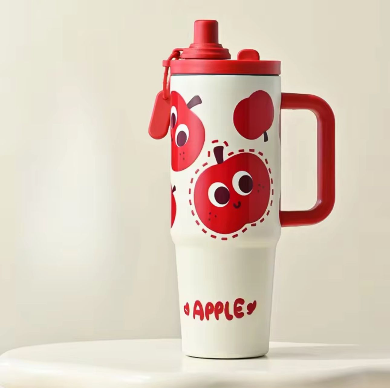 White tumbler with red apple design and handle on a beige background