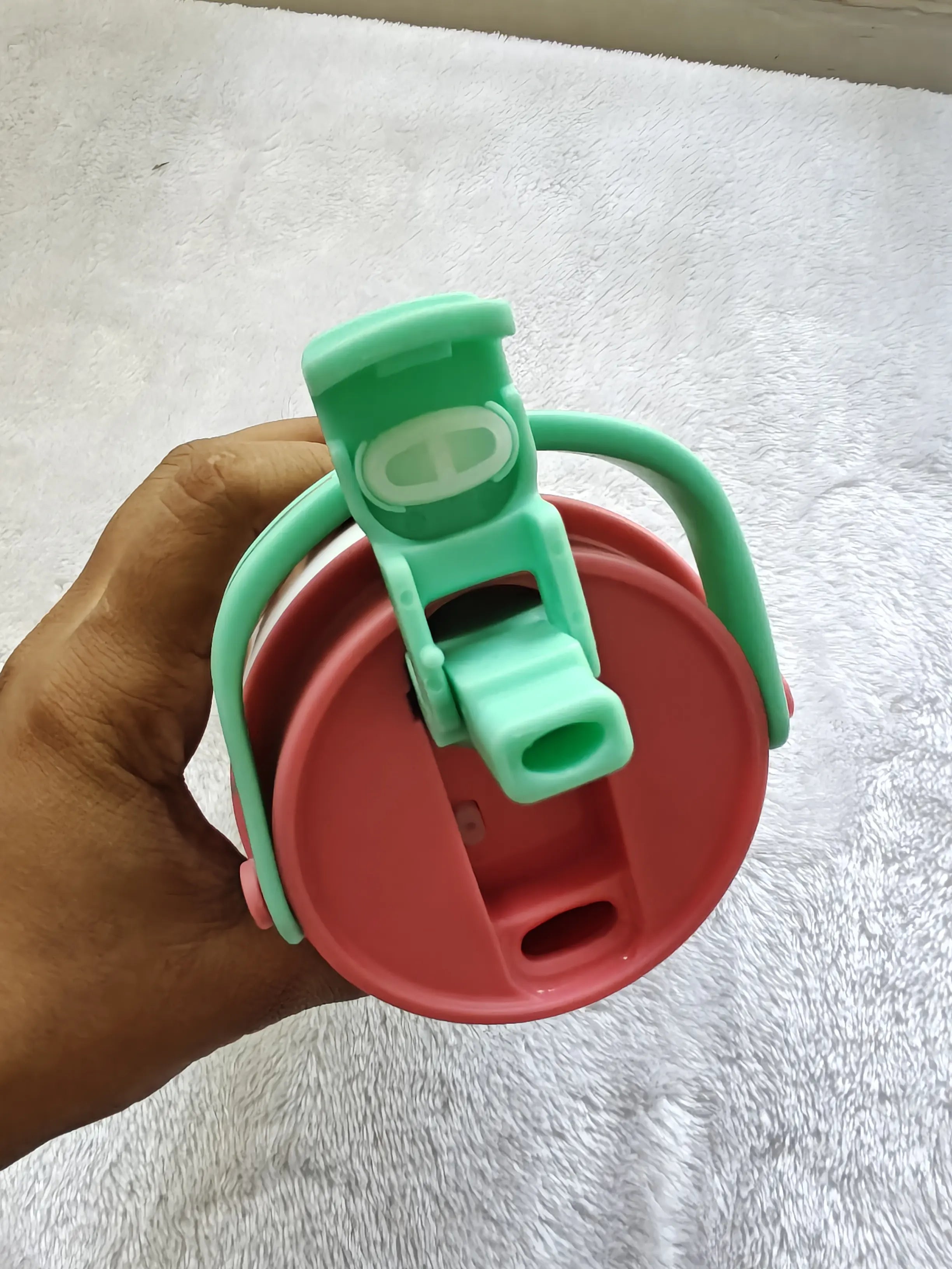 Hand holding a red and green container with a lid on a white towel background