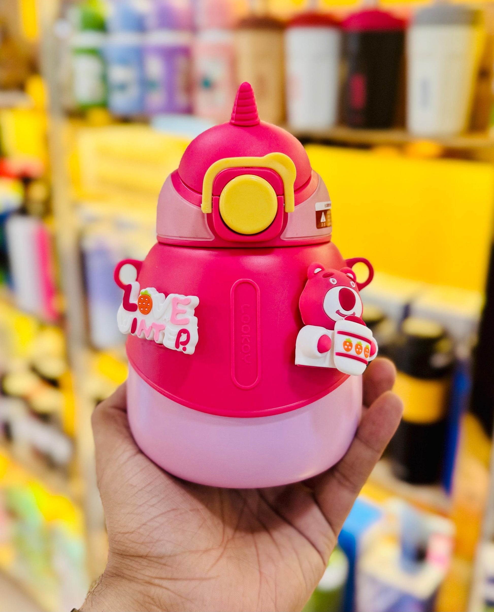 Pink cartoon-style water bottle held in a hand with a blurred store background