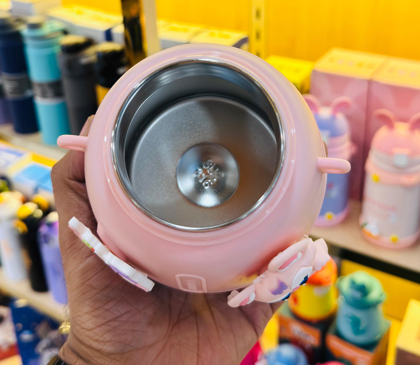 Pink thermos with a metal interior held in a hand against a colorful background