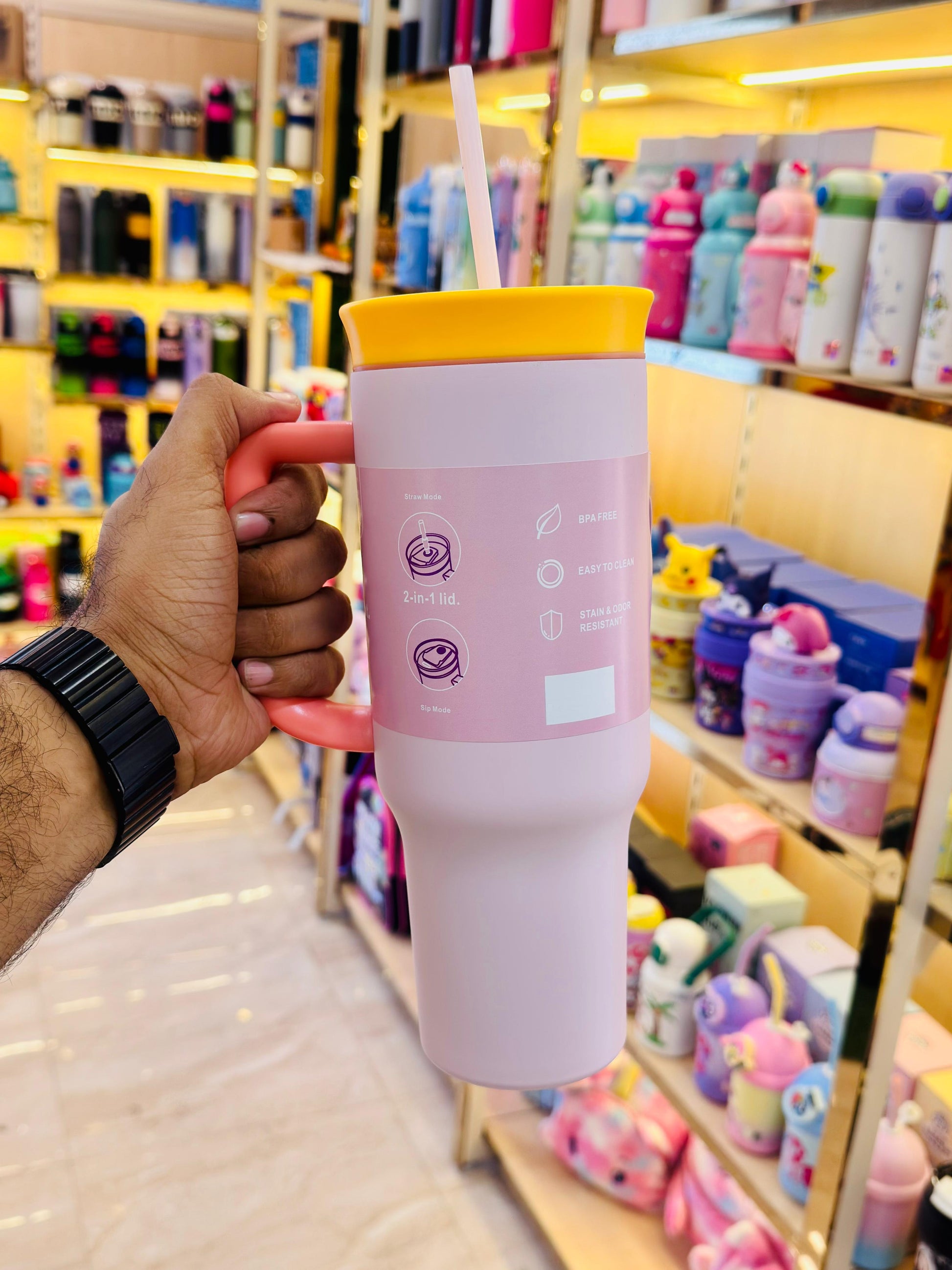 Pink tumbler with a yellow lid held in a hand against a store background