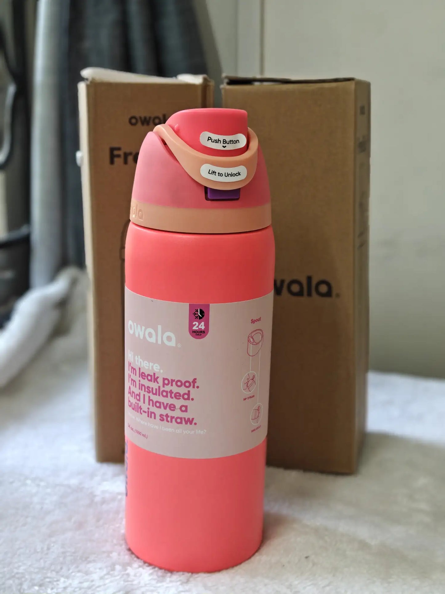 Pink insulated water bottle with a straw on a surface with a cardboard box in the background.