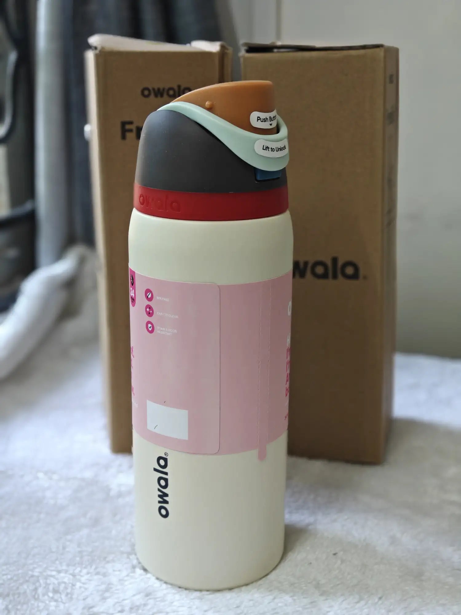 Owala water bottle with a pink label on a surface with a cardboard box in the background.