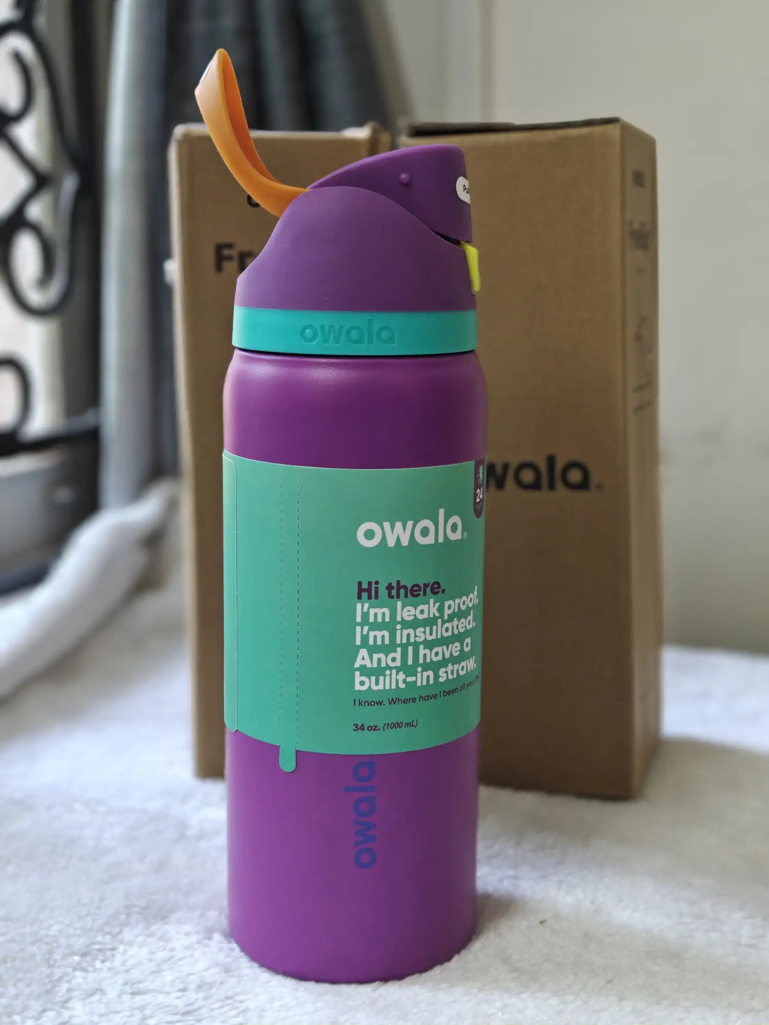 Purple and teal Owala water bottle with orange spout on a white surface.