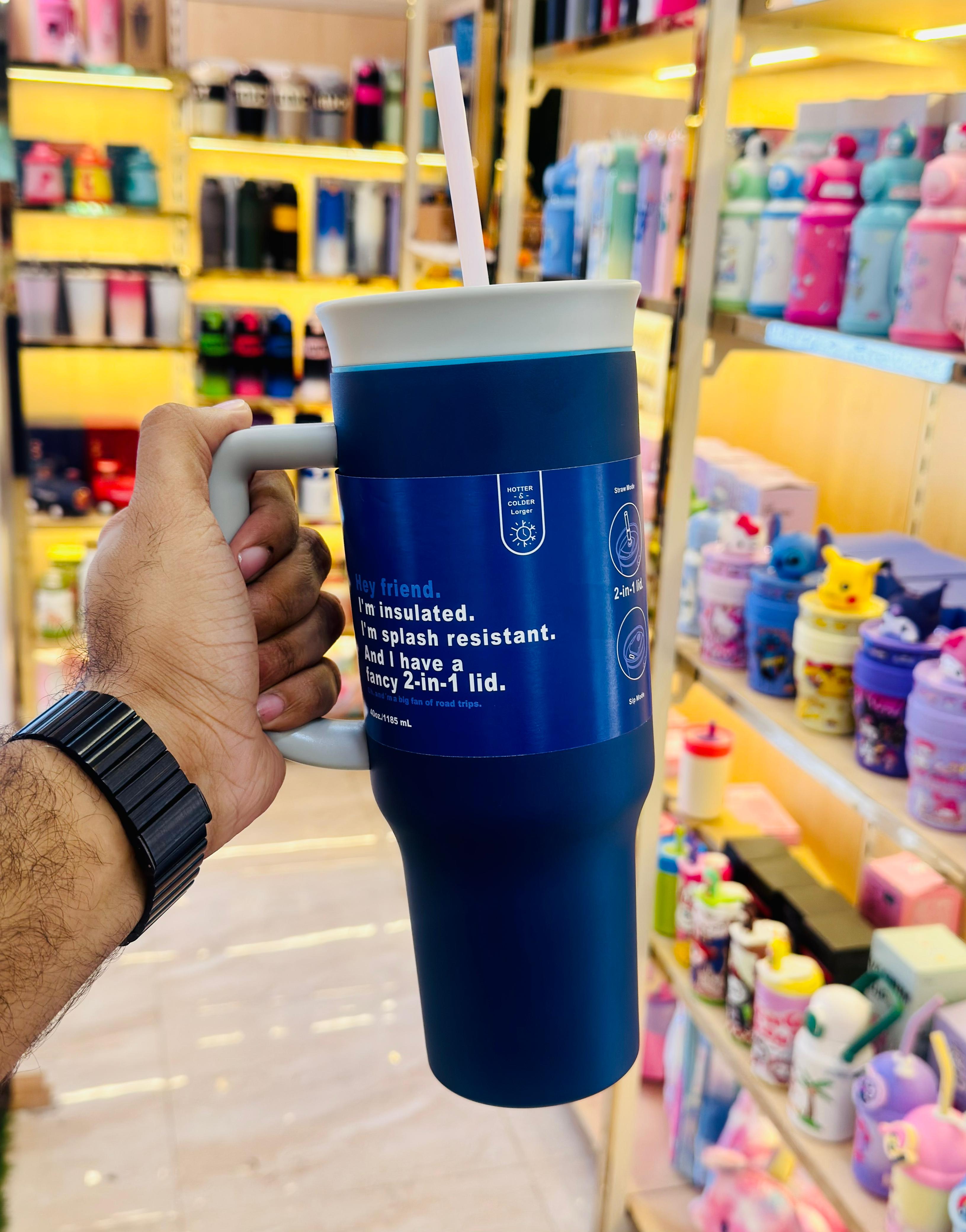 Blue insulated tumbler with a straw held by a hand in a store setting