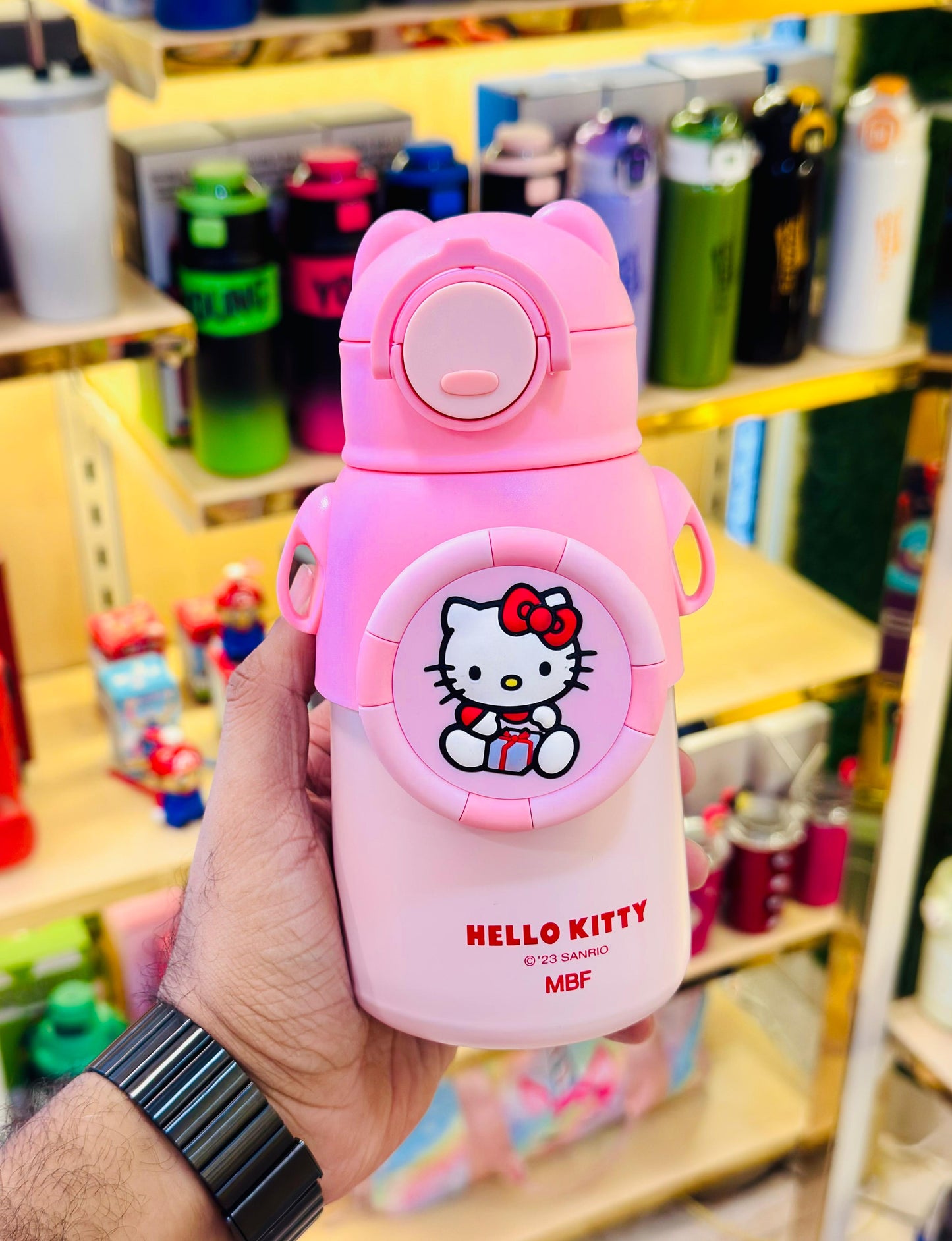 Pink Hello Kitty water bottle held by a person in a store setting with various bottles in the background.