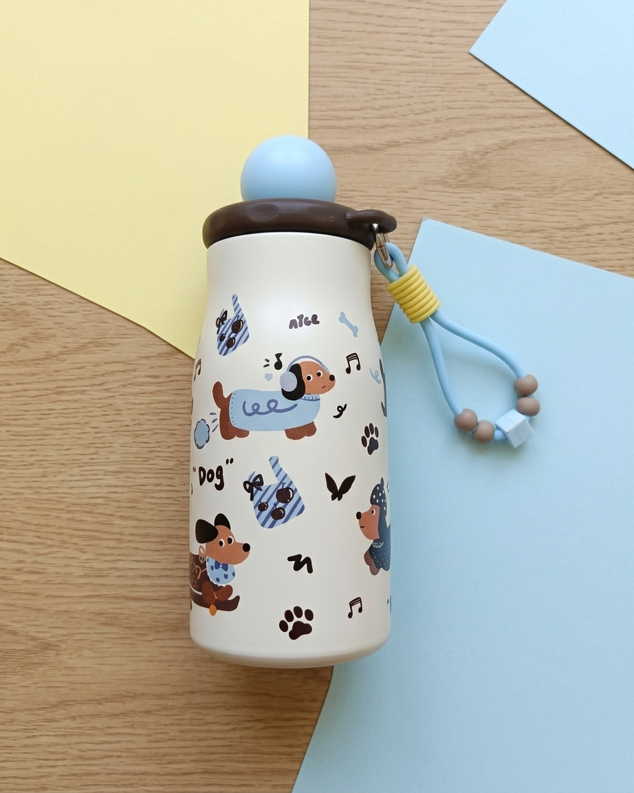 A cream-colored insulated water bottle with a dachshund cartoon pattern, a brown lid, and a light blue straw, displayed on a wooden surface with yellow and blue paper accents.