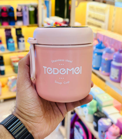 Pink soup cup with 'TODEMOI' branding held in a hand against a store background.