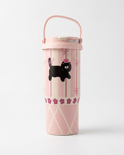 A pink travel tumbler with a matching handle lid, featuring a black cat illustration, pink bow and stripe patterns, and a floral band near the bottom, set against a plain light gray background.