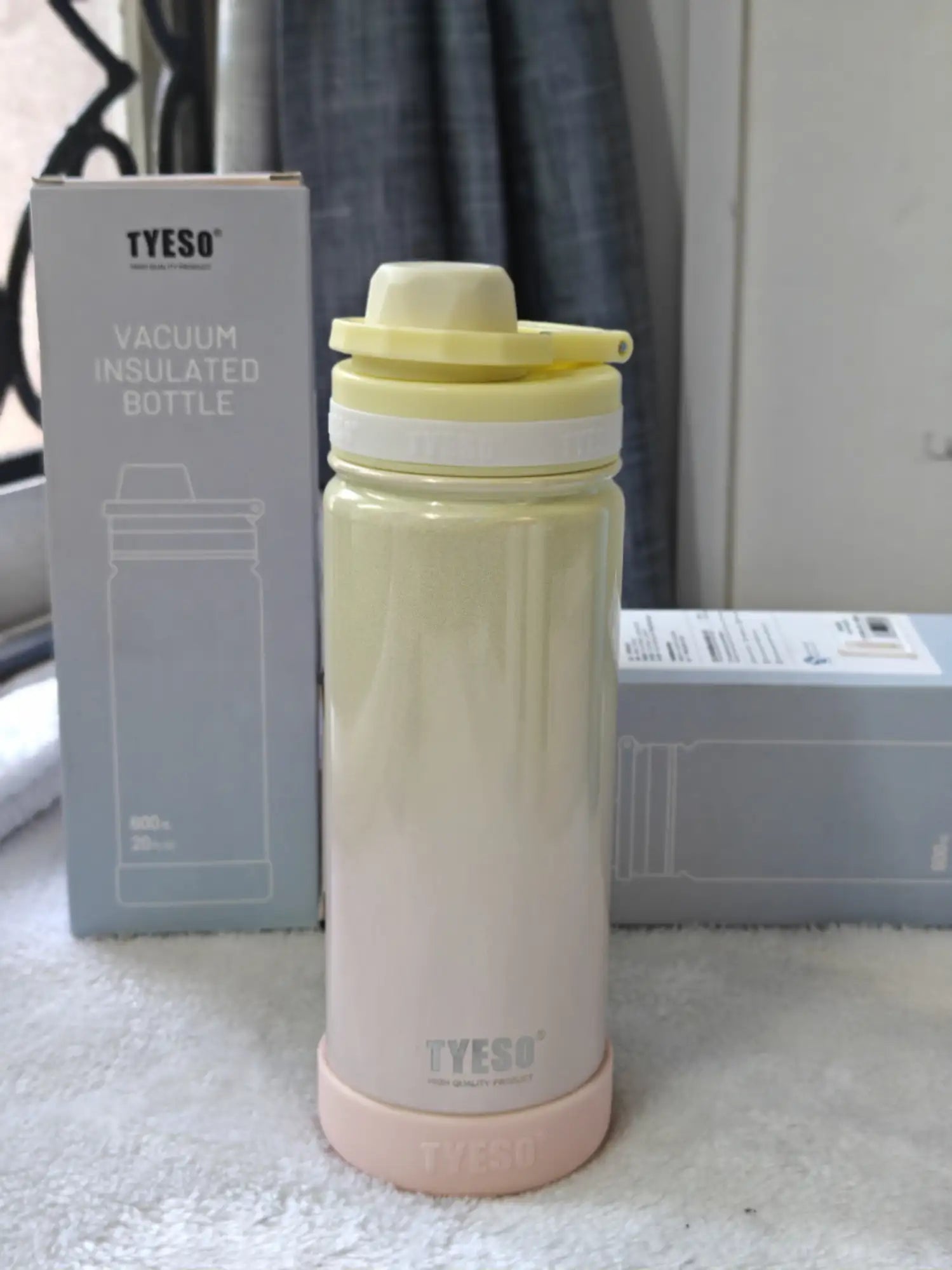 TYESO vacuum insulated bottle with pink base and yellow lid on a white surface.