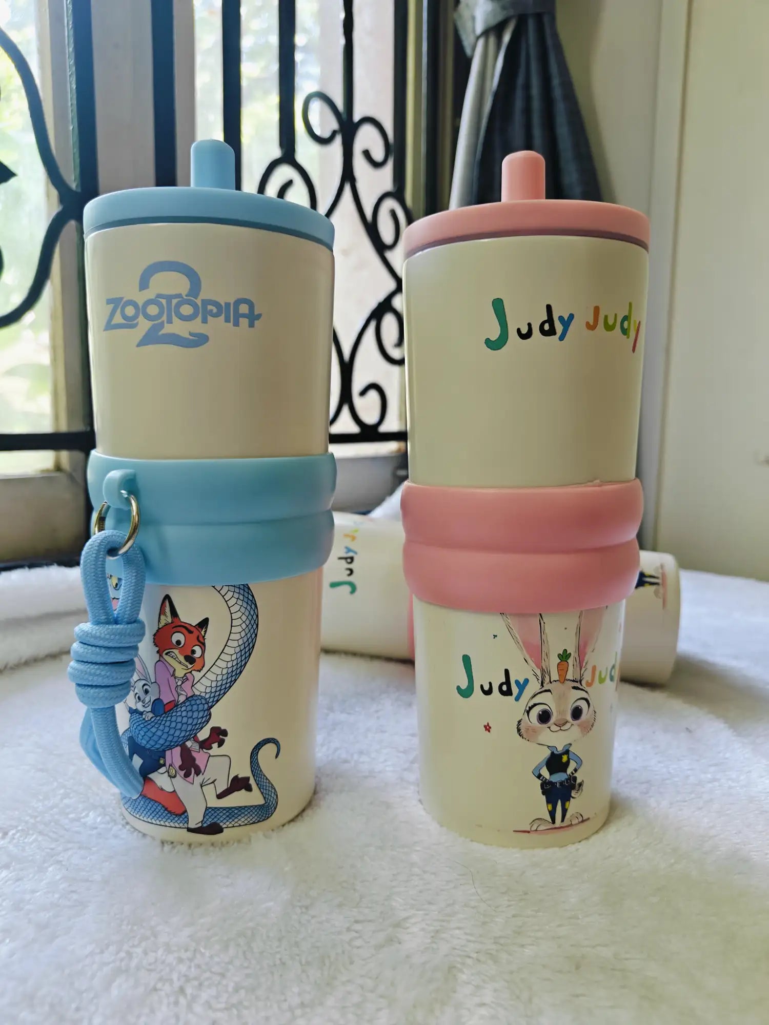 Two children's sippy cups with Zootopia and Judy designs on a white surface.
